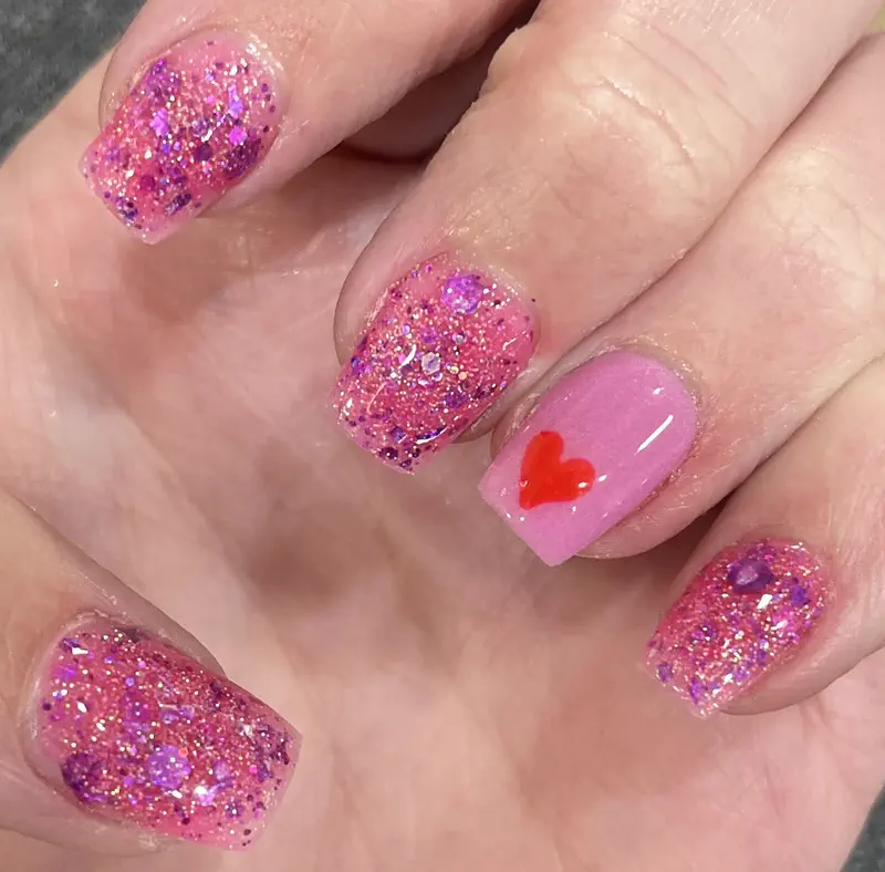 Short pink glitter nails with one red heart accent