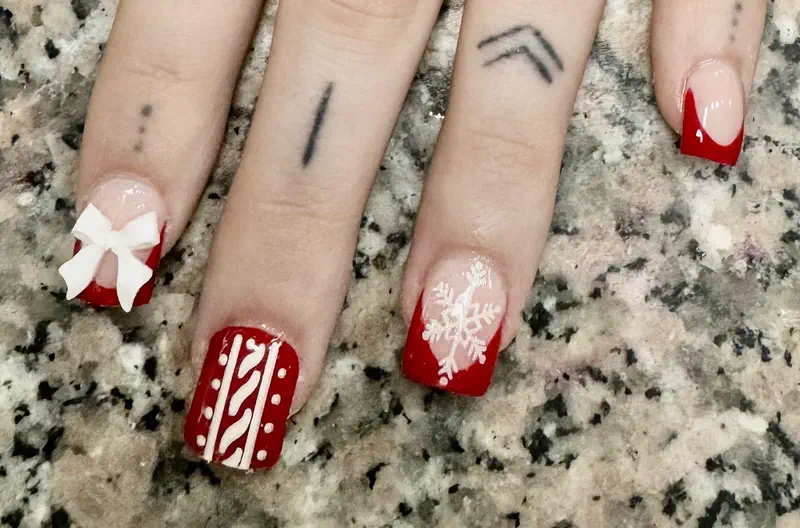 Short red French tips with a white bow, a hand-painted snowflake and a red knit-pattern nail